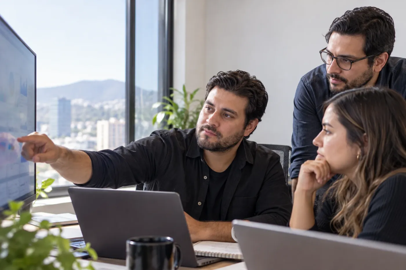 Fernando y dos especialistas de su equipo revisando un dashboard en una oficina con vista a la ciudad